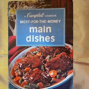 May include: A blue and white cookbook cover with the text "A Campbell Cookbook Most-For-The-Money main dishes". The cover features a photo of a plate of meat and vegetables.
