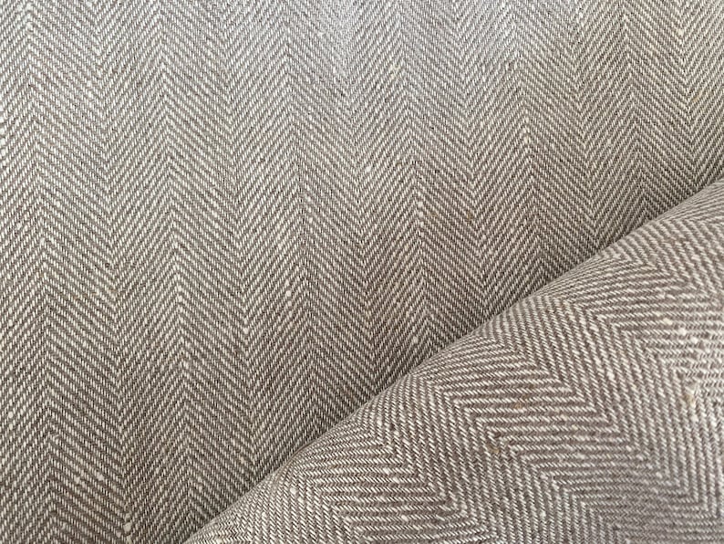 May include: Brown and white herringbone fabric with a subtle texture. The fabric is folded in half, showing the pattern on both sides.
