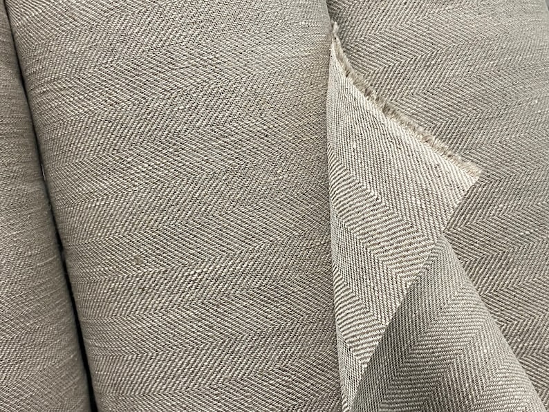 May include: Close-up of two rolls of gray herringbone fabric. The fabric has a subtle texture and a woven pattern.