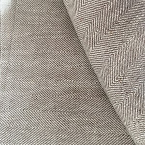 May include: Close-up of a brown and white herringbone fabric. The fabric is woven with a subtle texture and has a slightly rough feel.