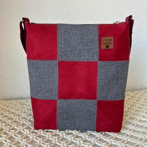 Könnte beinhalten: Schultertasche mit Patchwork-Muster in Rot und Grau mit Schachbrettmuster. Die Tasche hat einen Reißverschluss und ein braunes Lederetikett mit der Aufschrift "LANA WERK". Der Schulterriemen ist dunkelrot.