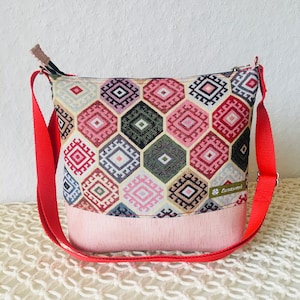 Könnte beinhalten: Eine rot-rosa gemusterte Umhängetasche mit rosa Stofffutter und einem roten verstellbaren Trageriemen. Die Tasche hat ein geometrisches Muster mit einem kleinen weißen Etikett mit der Aufschrift "Lanawerk".