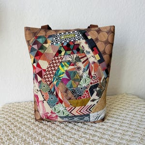 Könnte beinhalten: Eine bunte Patchwork-Tragetasche mit geometrischem Muster. Die Tasche ist aus verschiedenen Stoffen gefertigt und hat einen braunen Ledergriff.