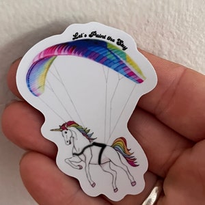 May include: A white unicorn with a rainbow mane and tail is attached to a colourful parachute with the text "Let's Paint the Sky".