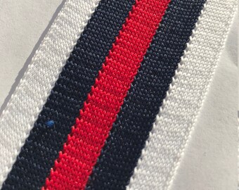 May include: White, red, and navy blue striped fabric trim. The trim is woven with a textured pattern.