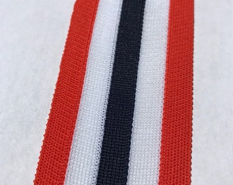 May include: Red, white, and navy blue striped elastic trim. The trim is woven with a textured pattern.