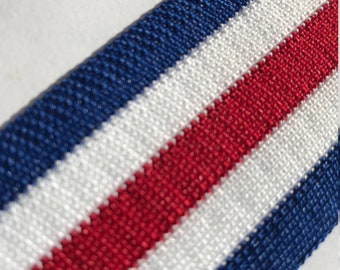 May include: Red, white, and blue striped fabric ribbon. The ribbon is woven with a textured pattern.