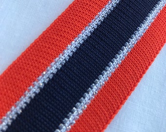 May include: Orange and navy blue fabric ribbon with a silver glitter trim. The ribbon is woven with a textured pattern.