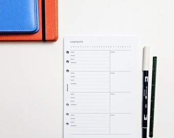 以下が含まれることがあります： 「CONTACTS」という文字が上部に書かれた白いページ。ページは4つのセクションに分かれており、名前、電話番号、メールアドレス、住所、メモの欄があります。白い表面に黒いマーカーが2本と白いマーカーが1本あります。