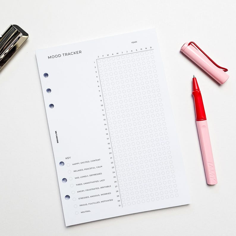 a mood tracking form with a grid layout, accompanied by a red pen and a black stapler on a white background.