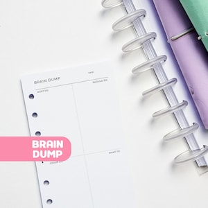 May include: A white planner insert with the words "Brain Dump" and sections for "Must Do," "Should Do," and "Want To." The insert is next to a clear disc-bound binding and a purple planner cover.