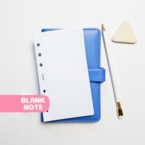 May include: A blue planner with a blank white page, a white pencil, and a triangular eraser. The words "BLANK NOTE" are in a pink banner. The planner is closed with a strap.