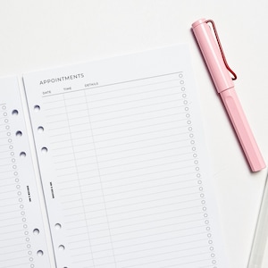 May include: A white appointment planner with the word "APPOINTMENTS" at the top. The planner has lines for date, time, and details. A pink pen with a red clip rests on the page.