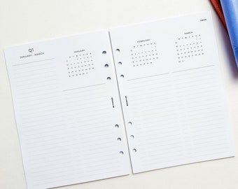 May include: A white planner with a black cover and a calendar for January, February, and March 2023. The planner has a Q1 label and the text "January - March".