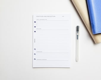 May include: A white paper planner insert with five holes on the left side. The page is titled Gratitude and Reflection and includes sections for Today I Am Grateful For, Reflection, Affirmations, and Tomorrow's Intentions with lines for writing.