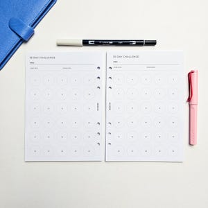a blue folder, a white 30-day challenge worksheet, a black pen, and a pink pen on a white background.