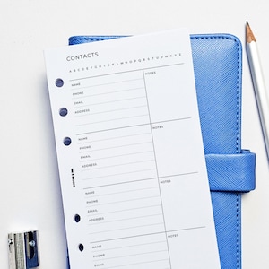 May include: A white contact list page with a blue binder. The page has a section for name, phone, email, and address, as well as a notes section. The page is labelled "CONTACTS" at the top and has the alphabet listed below.