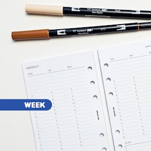 May include: Two Tombow ABT water-based markers, one beige and one brown, are positioned above a planner with weekly and monthly pages. The planner pages are white with a blue banner that says "WEEK".