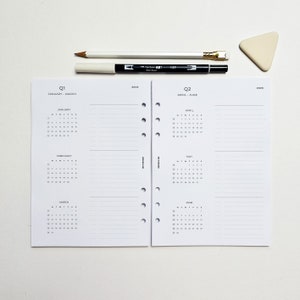 May include: A white planner with black text and a calendar for January through June. The planner is divided into two sections, one for Q1 and one for Q2. The planner has a hole punch on the left side and a spiral binding on the right side.