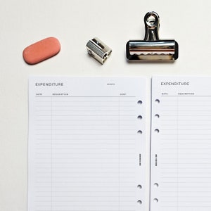May include: Two white pages with the word "EXPENDITURE" printed at the top. The pages are divided into three columns labelled "DATE", "DESCRIPTION", and "COST". The pages are bound together with a silver binder clip and have holes for a binder.