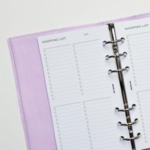 May include: A purple leather bound planner with a white page open to a shopping list. The page has two columns with check boxes and lines for writing. The planner has a silver ring binder.