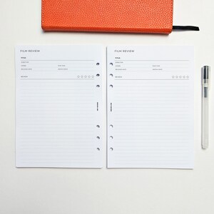 two blank film review forms with a pen and an orange notebook or folder on a white background.