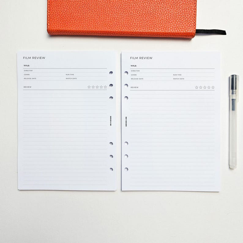 two blank film review forms with a pen and an orange notebook or folder on a white background.