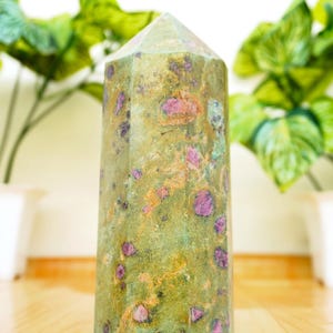 Peut inclure: Une pointe de cristal verte et rose avec une forme facetée. Le cristal a une texture naturelle, rugueuse et est parsemé d'inclusions roses et dorées.