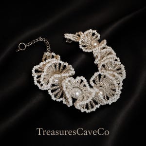 May include: A bracelet featuring a series of interconnected circular motifs crafted from small white beads and metallic silver thread. Each circular element contains a central white pearl-like bead. The bracelet includes a silver-tone metal chain.