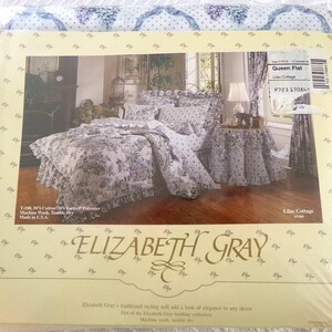 May include: A white and purple floral queen-sized flat sheet with a ruffled edge. The sheet is part of the Elizabeth Gray Lilac Cottage bedding collection. The packaging includes the product name, size, and care instructions.