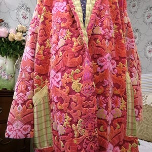 May include: A plush, floral-patterned robe in shades of red, pink, and orange. The robe features a shawl collar and pockets with a green plaid lining. The interior collar is a light green. The robe is a vintage style.