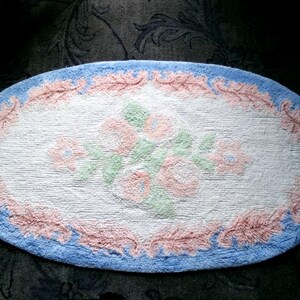May include: Oval shaped bath rug with a blue border, pink floral design, and a white background.