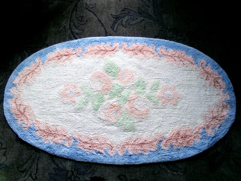 May include: Oval shaped bath rug with a blue border, pink floral design, and a white background.