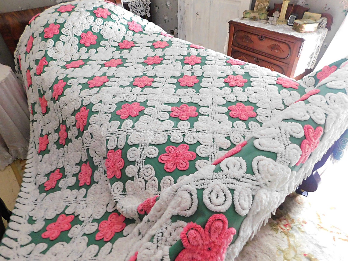May include: Vintage handmade quilted bedspread in teal green, featuring a floral pattern with pink and white flowers. The intricate design showcases raised, textured blossoms and leaves, creating a three-dimensional effect. The bedspread has a fringed edge, adding to its antique charm. This unique piece is ideal for adding a touch of vintage elegance to any bedroom.