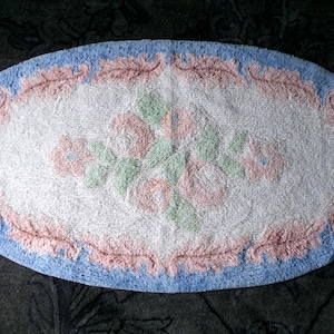 May include: Oval shaped bath mat with a blue border and a pink floral design in the center.