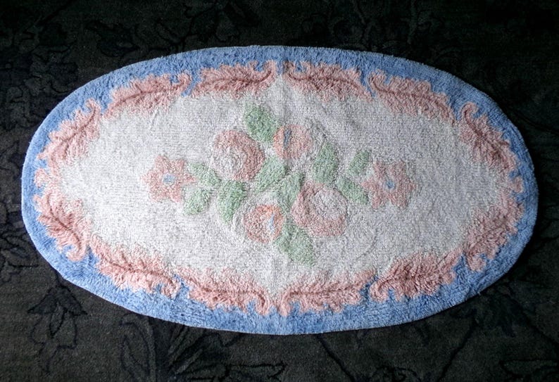 May include: Oval shaped bath mat with a blue border and a pink floral design in the center.