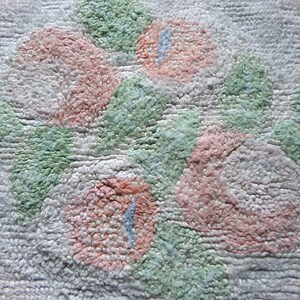 May include: A close-up of a white bath mat with a textured design of pink and green flowers. The mat is made of a soft, fluffy material.