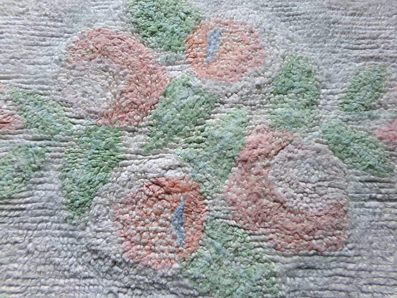 May include: A close-up of a white bath mat with a textured design of pink and green flowers. The mat is made of a soft, fluffy material.