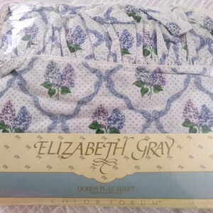 May include: A white queen flat sheet with a lilac floral pattern and blue ribbon design. The sheet is packaged and labeled "Elizabeth Gray" and "Colorforum".