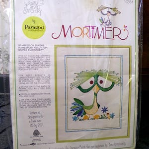 May include: A vintage "Mortimer" embroidery kit by Paragon Needlecraft. The kit includes a stamped picture of a whimsical bird with green, yellow, and blue details, designed to fit a 16 x 20 inch frame. The kit contains wool yarn, needle, and instructions.