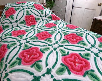 May include: A white tufted bedspread featuring a repeating pattern of raised pink floral motifs and green leaf accents. The textured design consists of interconnected loops and tufted yarn, creating a dimensional surface across the entire fabric.
