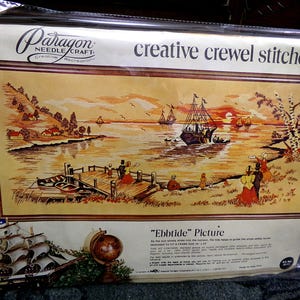 May include: A vintage "Ebb Tide" picture needlecraft kit. The image depicts a coastal scene with sailboats, a pier, and figures in period clothing. The kit is packaged in a clear plastic sleeve, with the text "creative crewel stitchery" at the top.