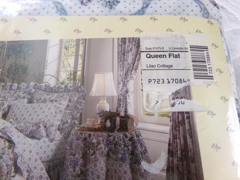 May include: A queen-sized flat sheet in a lilac floral pattern. The sheet is shown on a bed with matching pillowcases and a throw blanket. The sheet is labeled "Queen Flat" and "Lilac Cottage".
