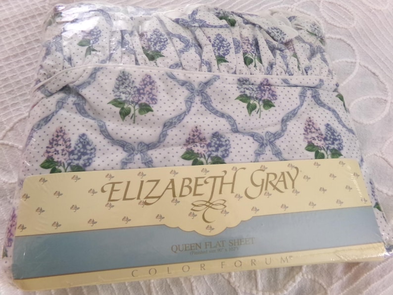 May include: A white queen flat sheet with a blue and white floral pattern. The sheet is packaged and labeled "Elizabeth Gray" and "Color Forum".