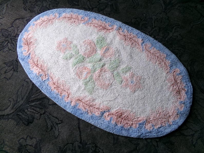 May include: Oval shaped bath mat with a pink and blue floral design. The mat is white in the center with a pink and blue border.