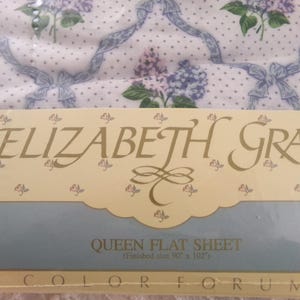May include: A white flat sheet with a floral pattern in shades of purple and green. The sheet is labeled "ELIZABETH GRAY QUEEN FLAT SHEET (Finished size 90 x 102") COLOR FORUM".