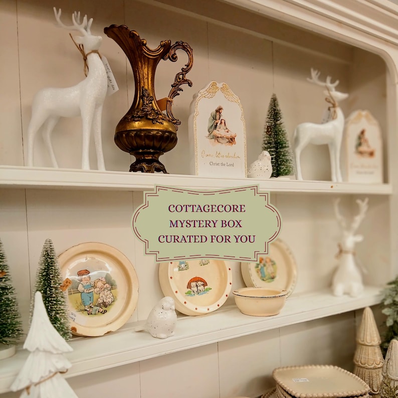 Puede incluir: Una exhibici&oacute;n de decoraci&oacute;n cottagecore en estantes blancos. Los art&iacute;culos incluyen figuras de ciervos blancos, platos decorativos con ilustraciones, un jarr&oacute;n dorado, peque&ntilde;os &aacute;rboles de Navidad y un letrero que dice "COTTAGECORE MYSTERY BOX CURATED FOR YOU."