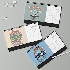 May include: Desktop calendars with spiral binding. Each calendar features a different month and a unique design with inspirational text and retro graphics. The calendars are displayed on a grey surface with binder clips.