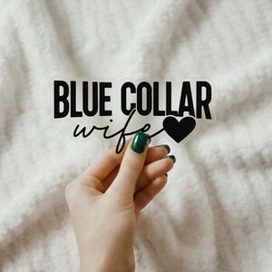 以下が含まれることがあります： 太い黒のサンセリフ体で「BLUE COLLAR」というテキストが書かれ、その後に黒の筆記体で「wife」という単語と塗りつぶされた黒いハートのアイコンが続く、透明な素材に貼られたダイカットビニールステッカー。