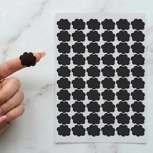 May include: A sheet of black, cloud-shaped stickers. One sticker is on a finger. The stickers are arranged in rows and columns on a white background. The stickers are a matte black color.